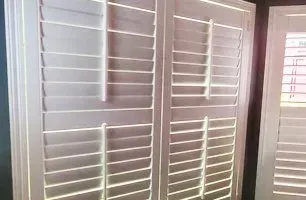 White wooden interior shutters, closed, with angled slats allowing light to pass through.