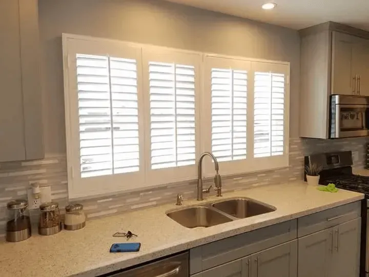 Kitchen with white shutters over a double sink, light countertops, and gray cabinets.