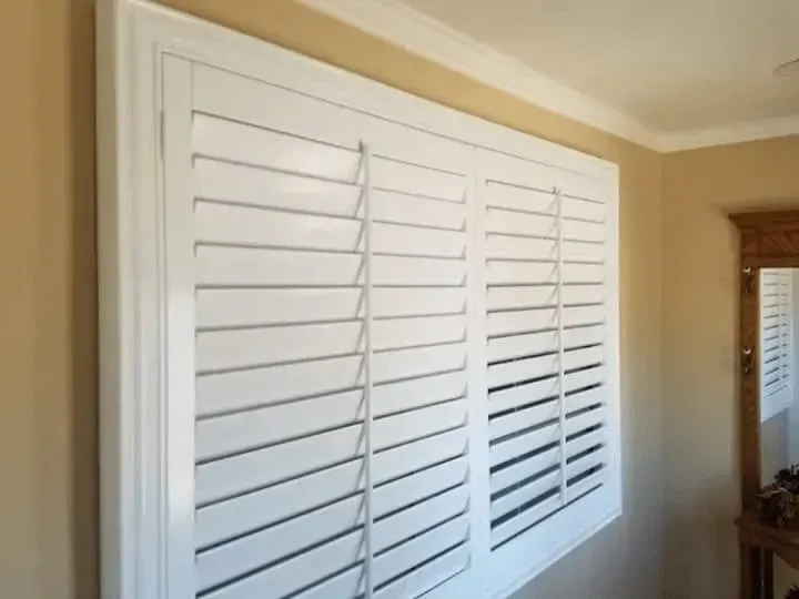 White plantation shutters covering a window in a beige-walled room.