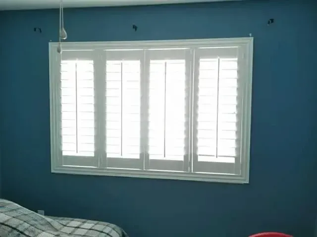 White shutters on a window with blue wall in a bedroom.
