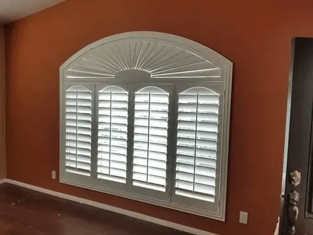 White shuttered window in an orange room with an arched top.