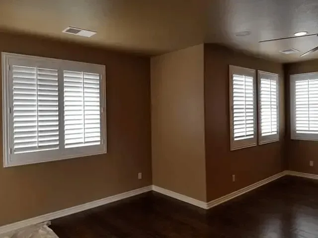 Room with brown walls, white shuttered windows, and dark wood floor.