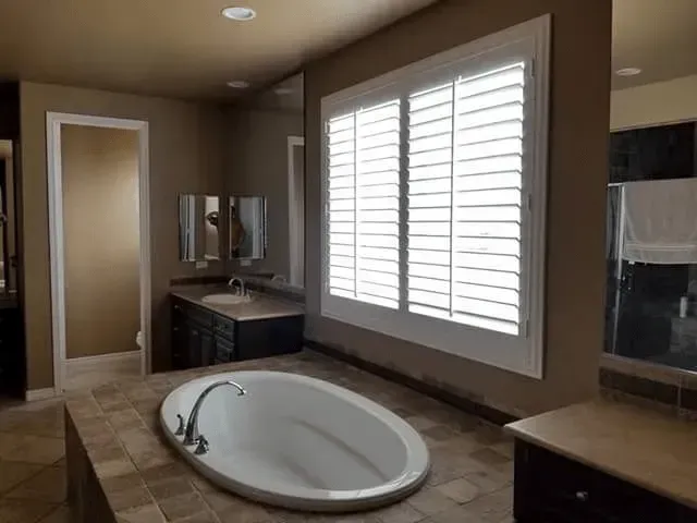 Bathroom with an oval tub, shutters on window, dark vanity, and tiled floors.