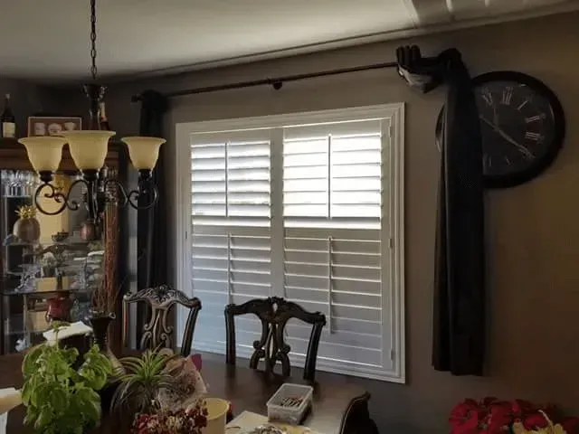 White shutters on a window in a dining room, with a dark brown curtain rod.