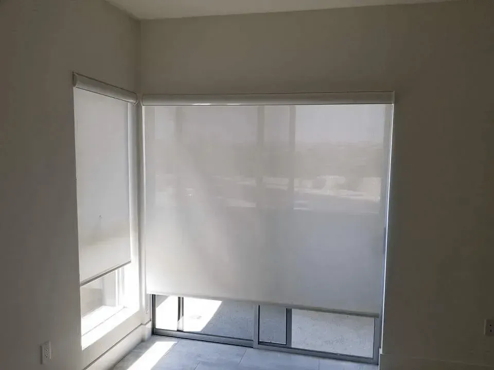 White roller blinds cover windows in a corner room.