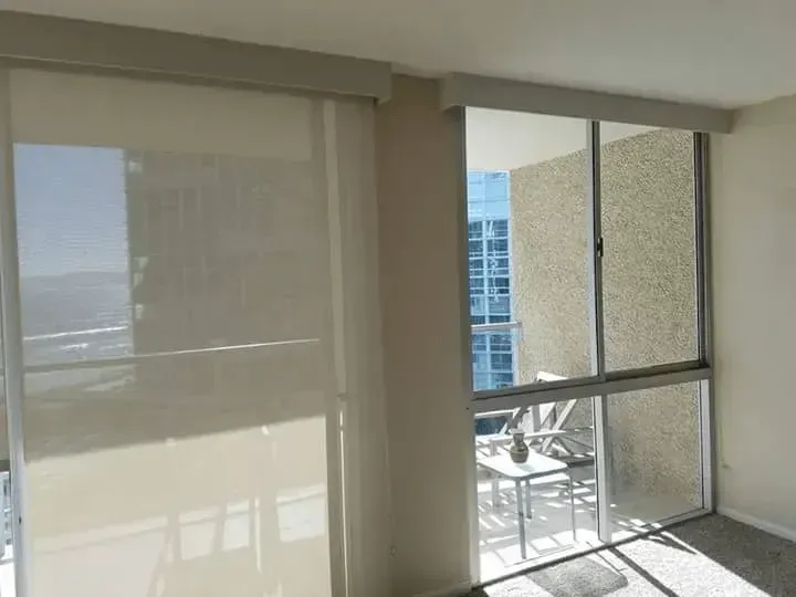 Beige roller shades on a window and sliding glass door, with a balcony view.