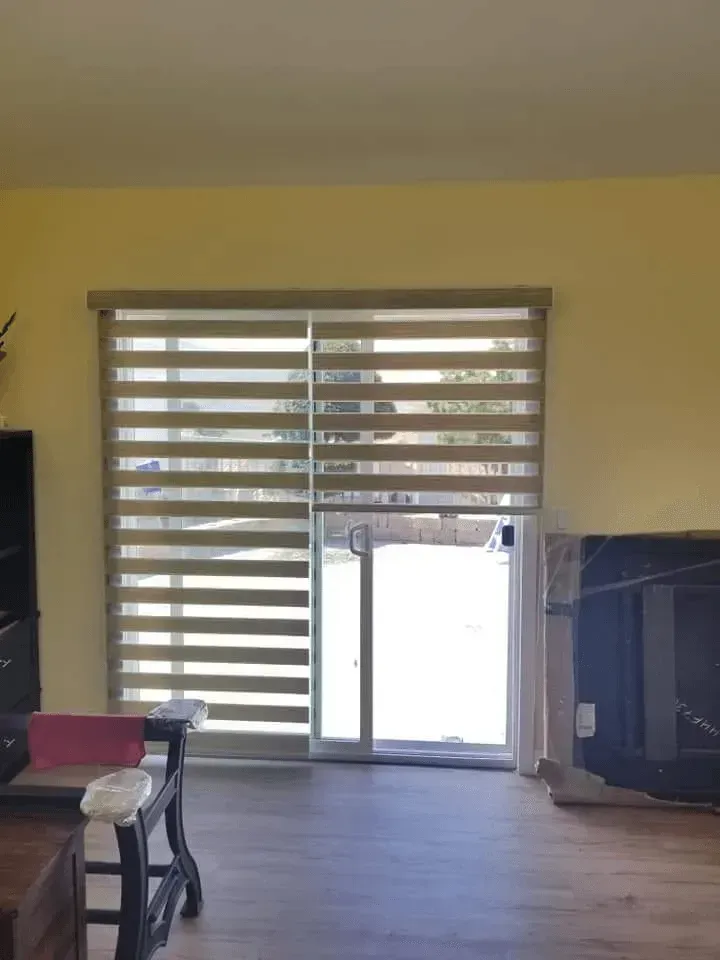 Beige and cream striped window blinds over a sliding glass door, in a yellow-walled room.