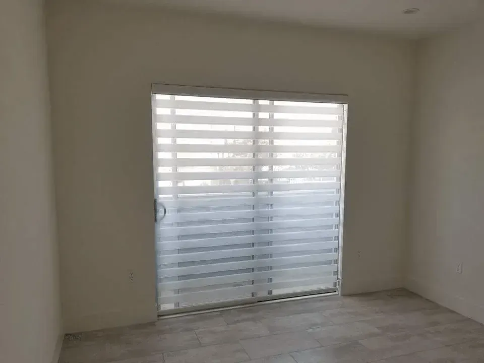 Empty room with a large sliding glass door covered by white horizontal blinds.