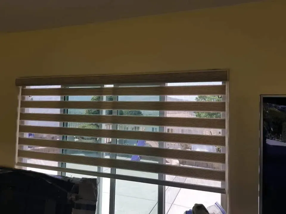 Window with horizontal striped blinds, beige and clear sections, against a yellow wall.