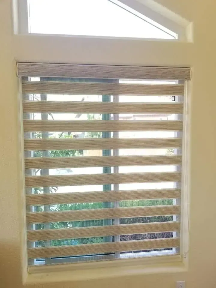 Window with layered blinds, beige and white stripes, in a room with a small triangular window above.