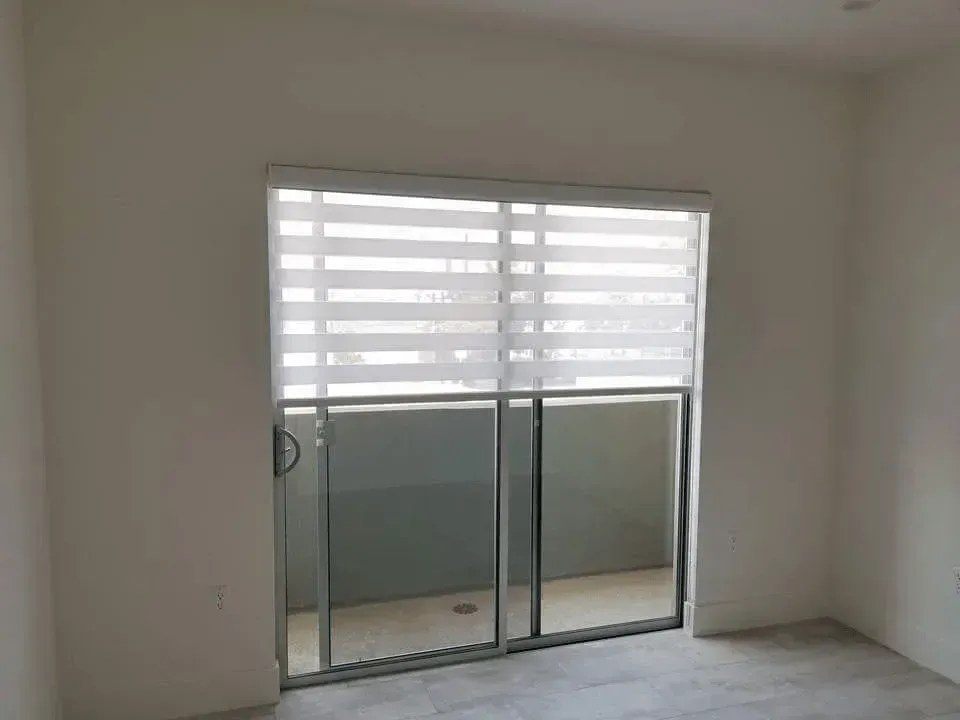 Sliding glass door with white sheer blinds, leading to a balcony. Room has white walls and a gray floor.