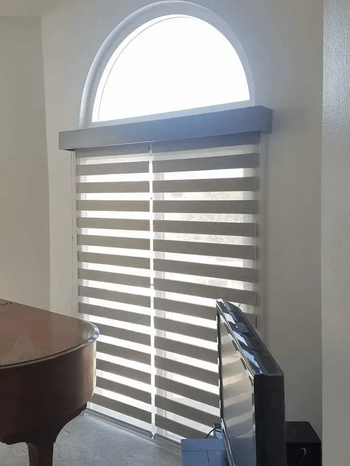 A window with layered blinds and an arched top, in front of a piano.
