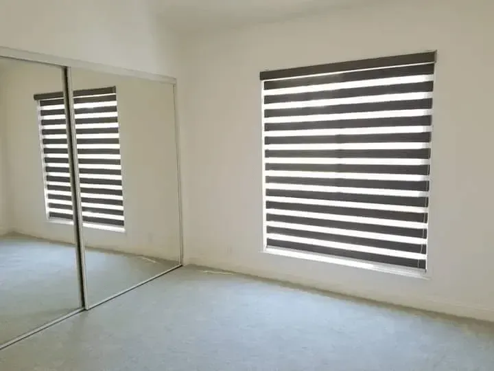 Empty room with large window and mirror, both with zebra blinds.