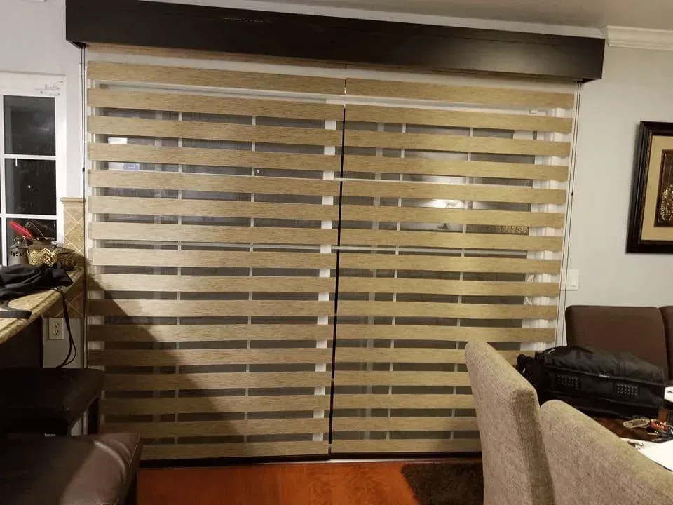 Beige horizontal blinds covering a sliding glass door and window. Wooden floor and brown trim.