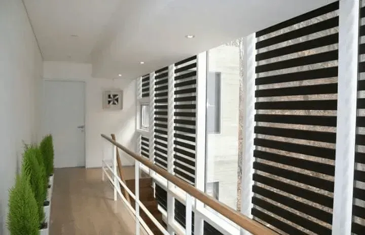 Hallway with striped shades, railing, plants, and door.