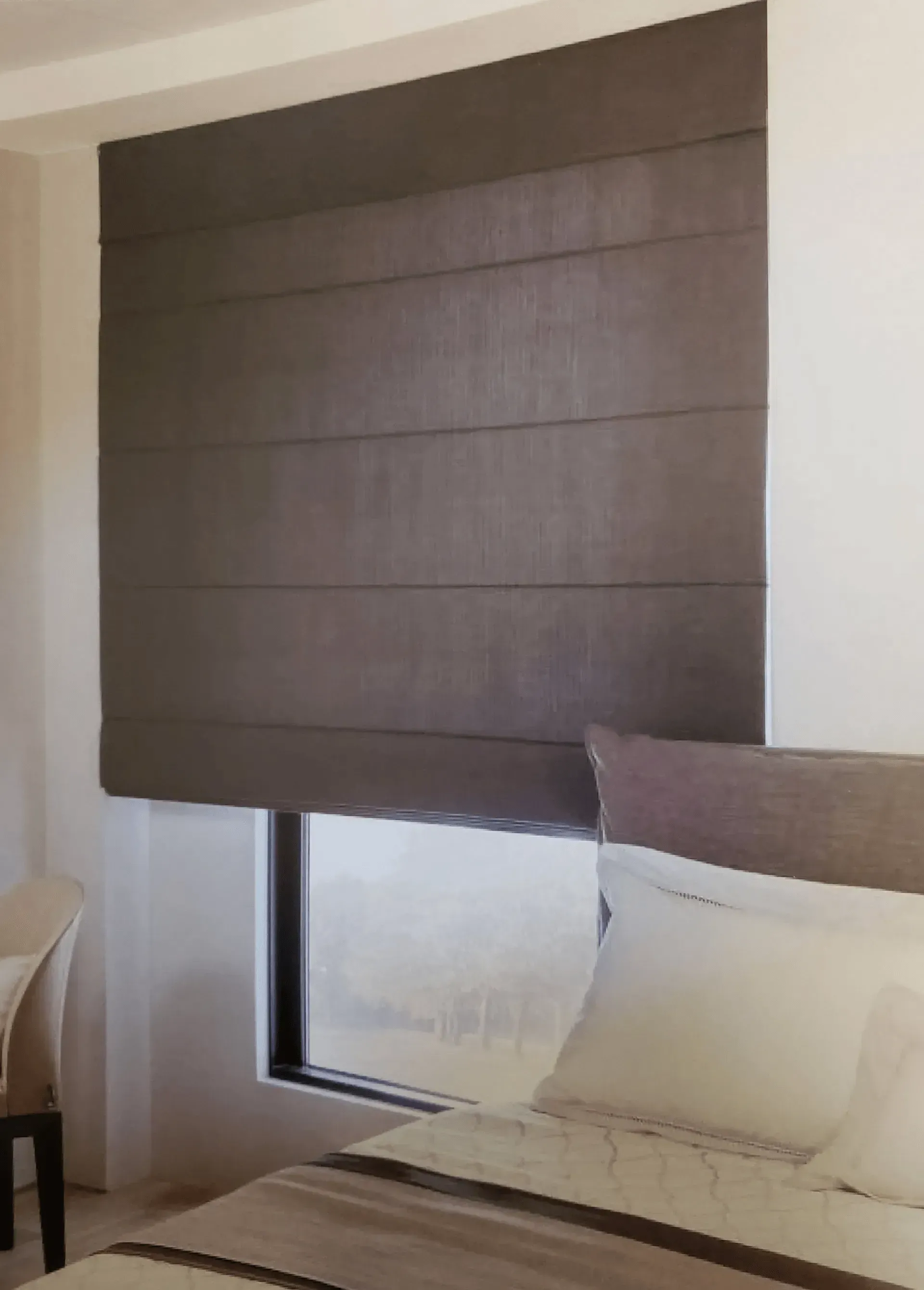 Dark brown Roman shade over a window in a bedroom, partially obscuring the view of the outdoors.