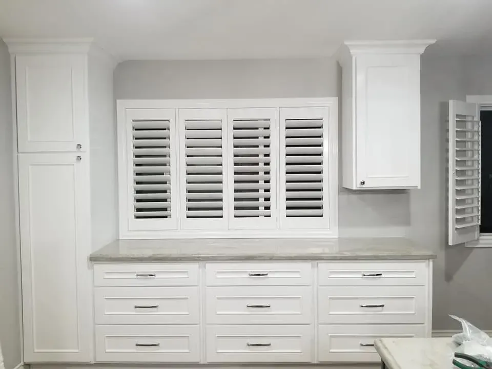 White kitchen cabinets with drawers and shutters, gray countertop, and tall pantry.