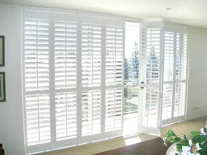 White interior shutters, partially open, provide a view of the outside and allow sunlight to enter.