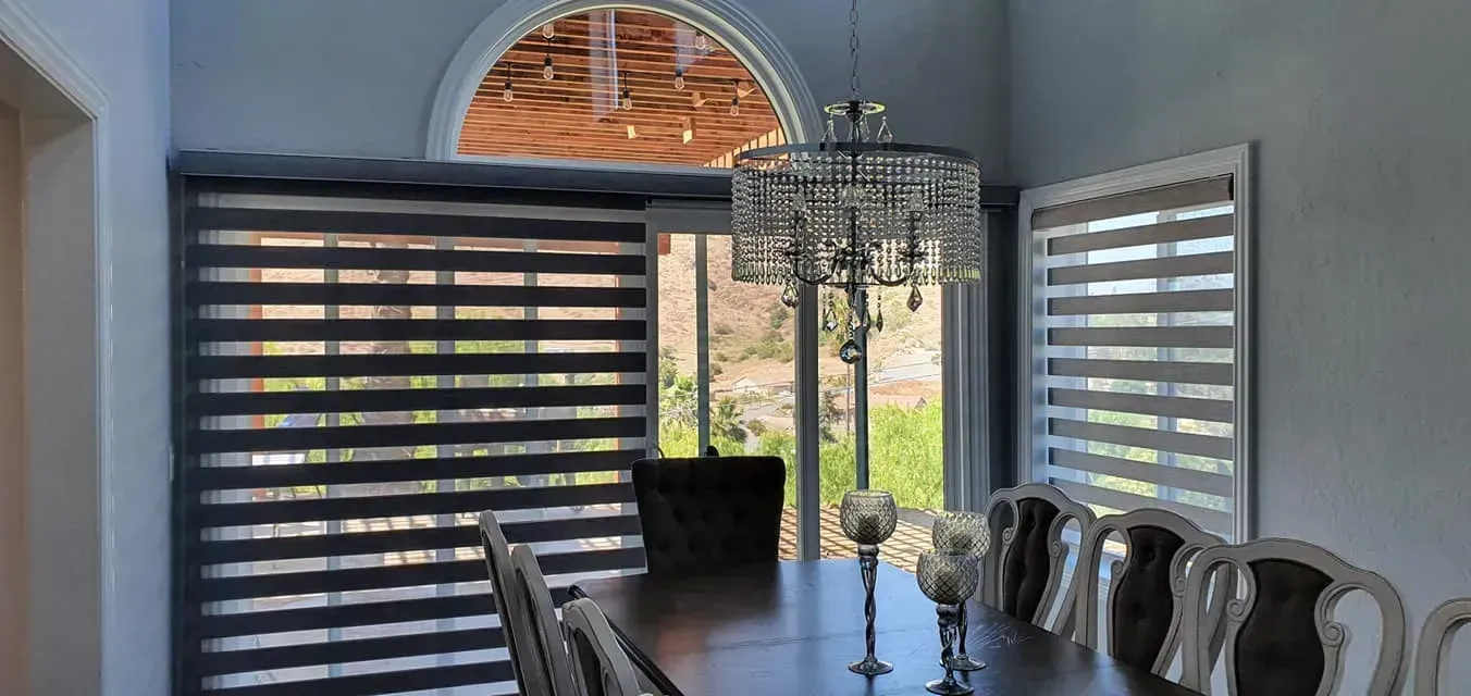 Dining room with dark wood table, chairs, chandelier, and window blinds.