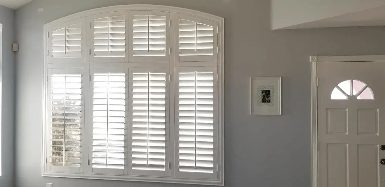 White window shutters with arched top, gray wall, a framed picture, and a white door.