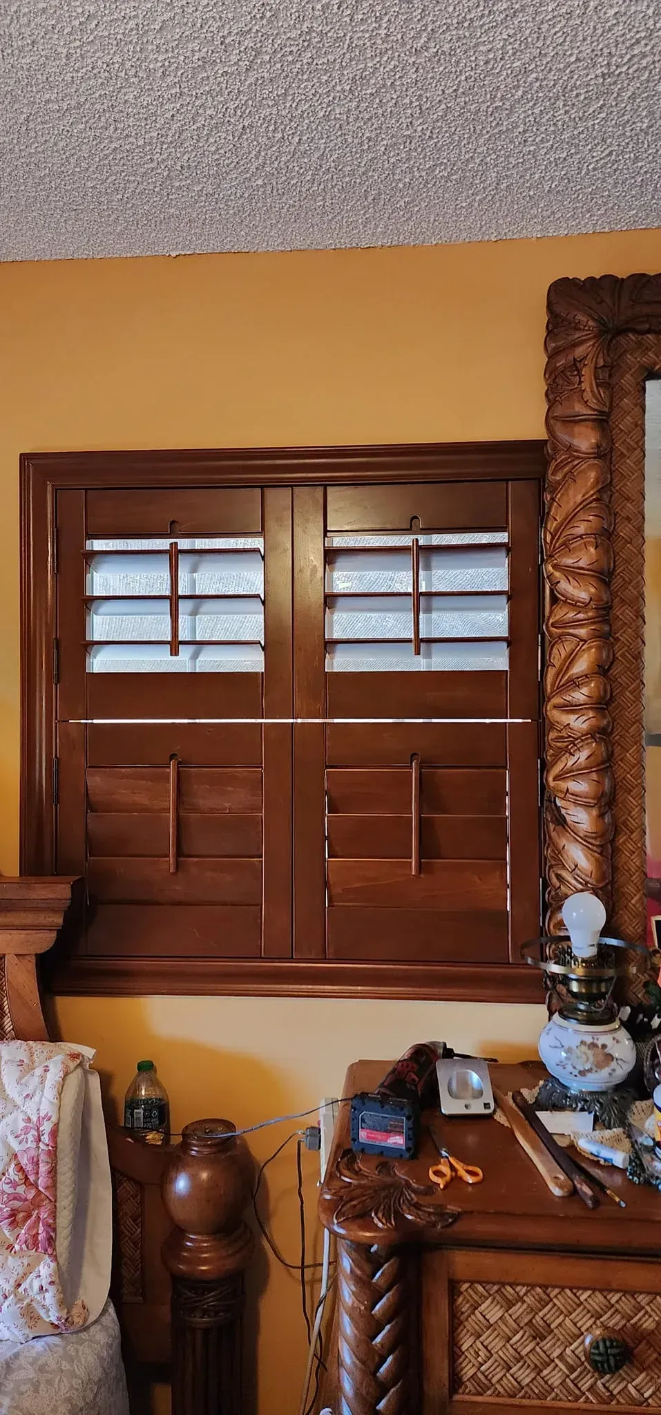 Wooden window shutters on a gold wall, surrounded by furniture and a mirror.