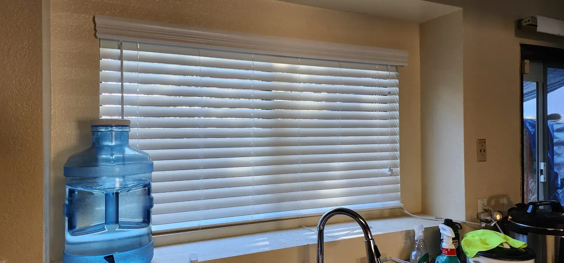 Window with white blinds, a water cooler, and kitchen sink.