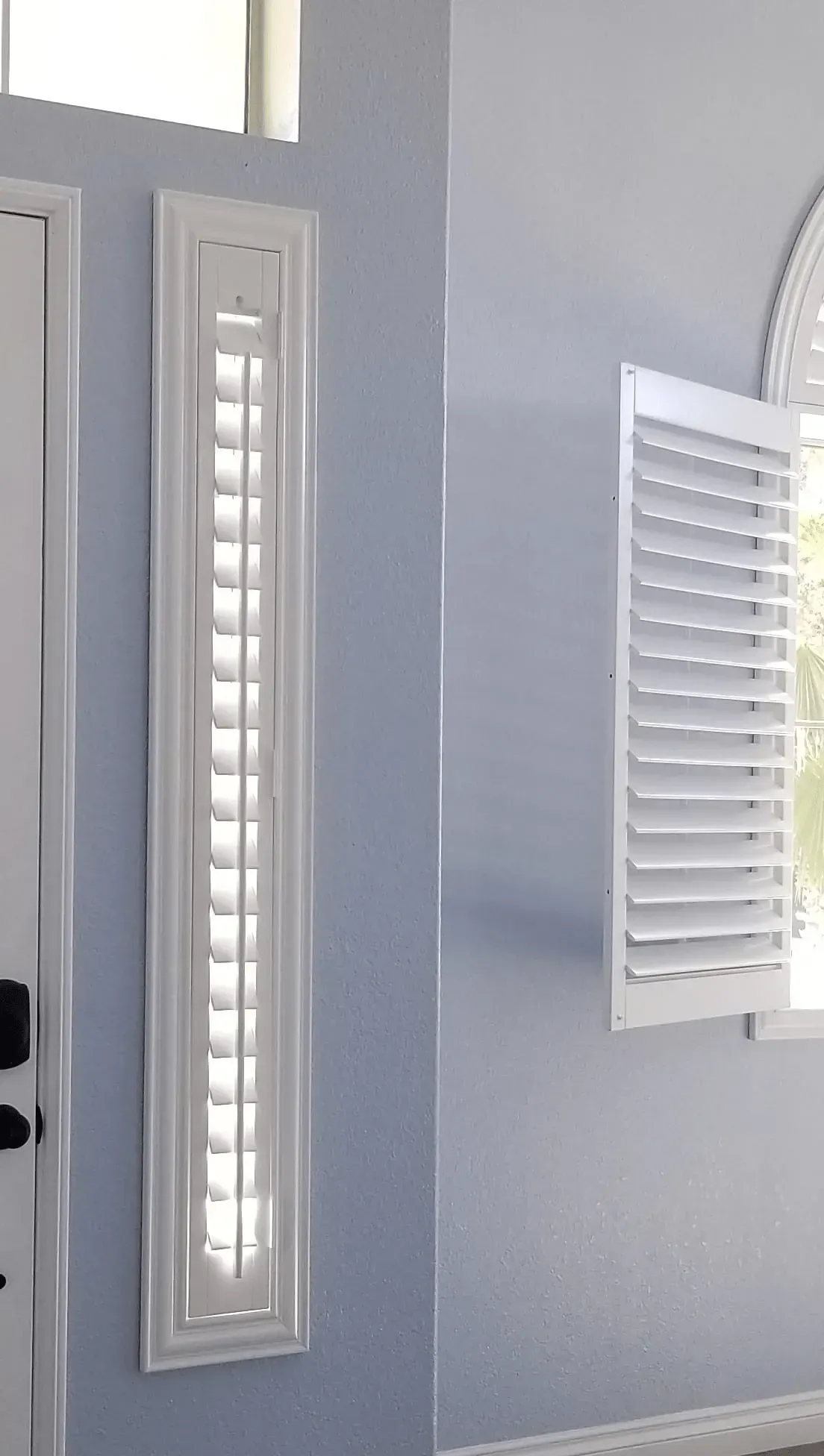 White shutters on a narrow wall and a window, both with open slats, beside a doorway.