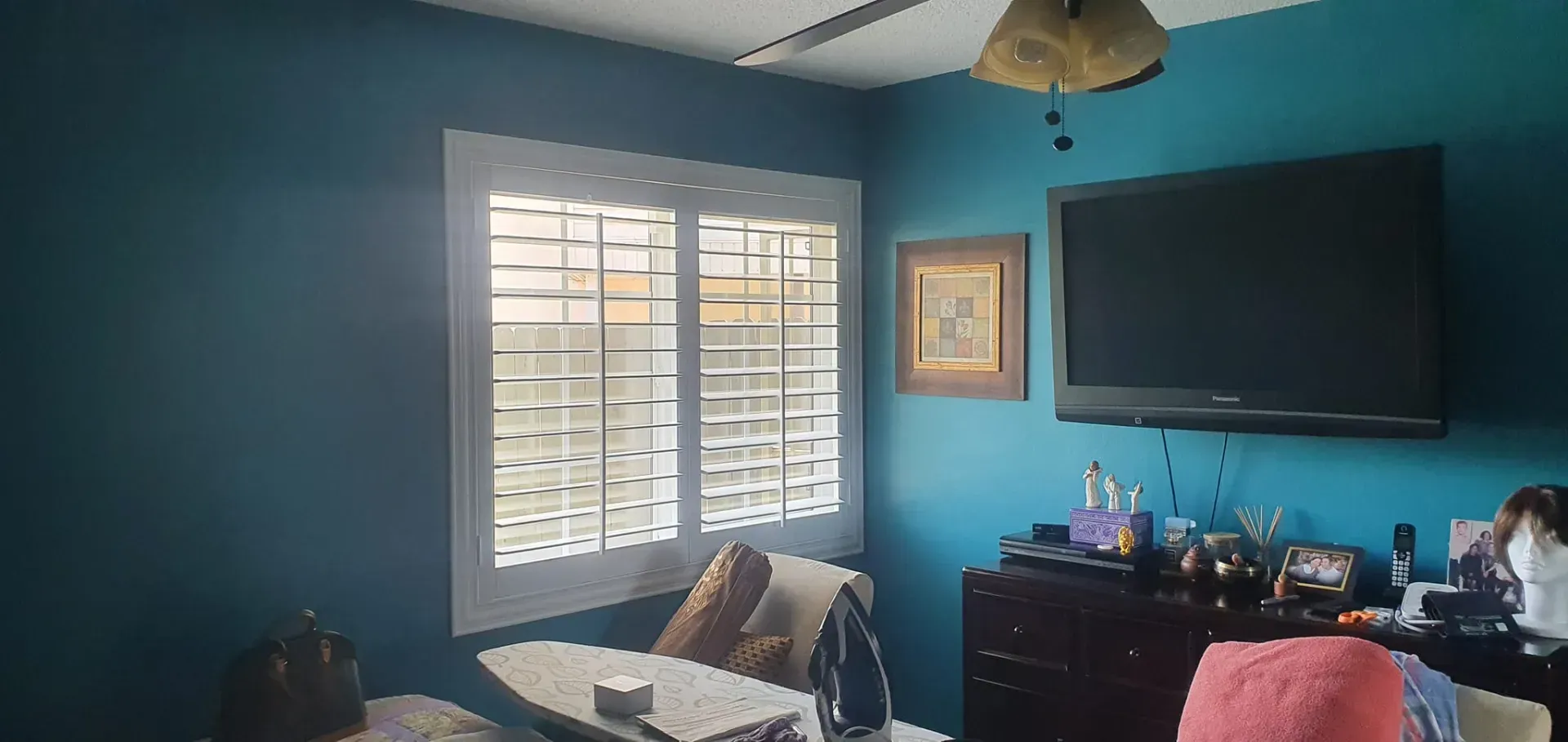 A room with teal walls, a white-framed window, a TV, and furniture.