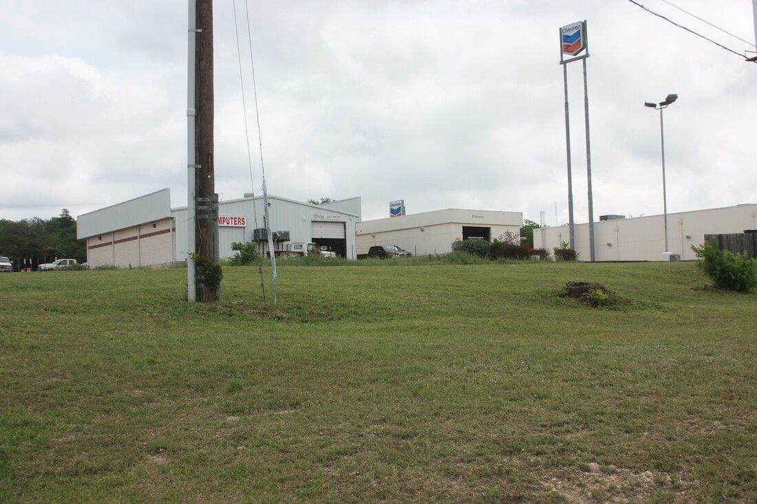 A large white building is sitting in the middle of a grassy field.