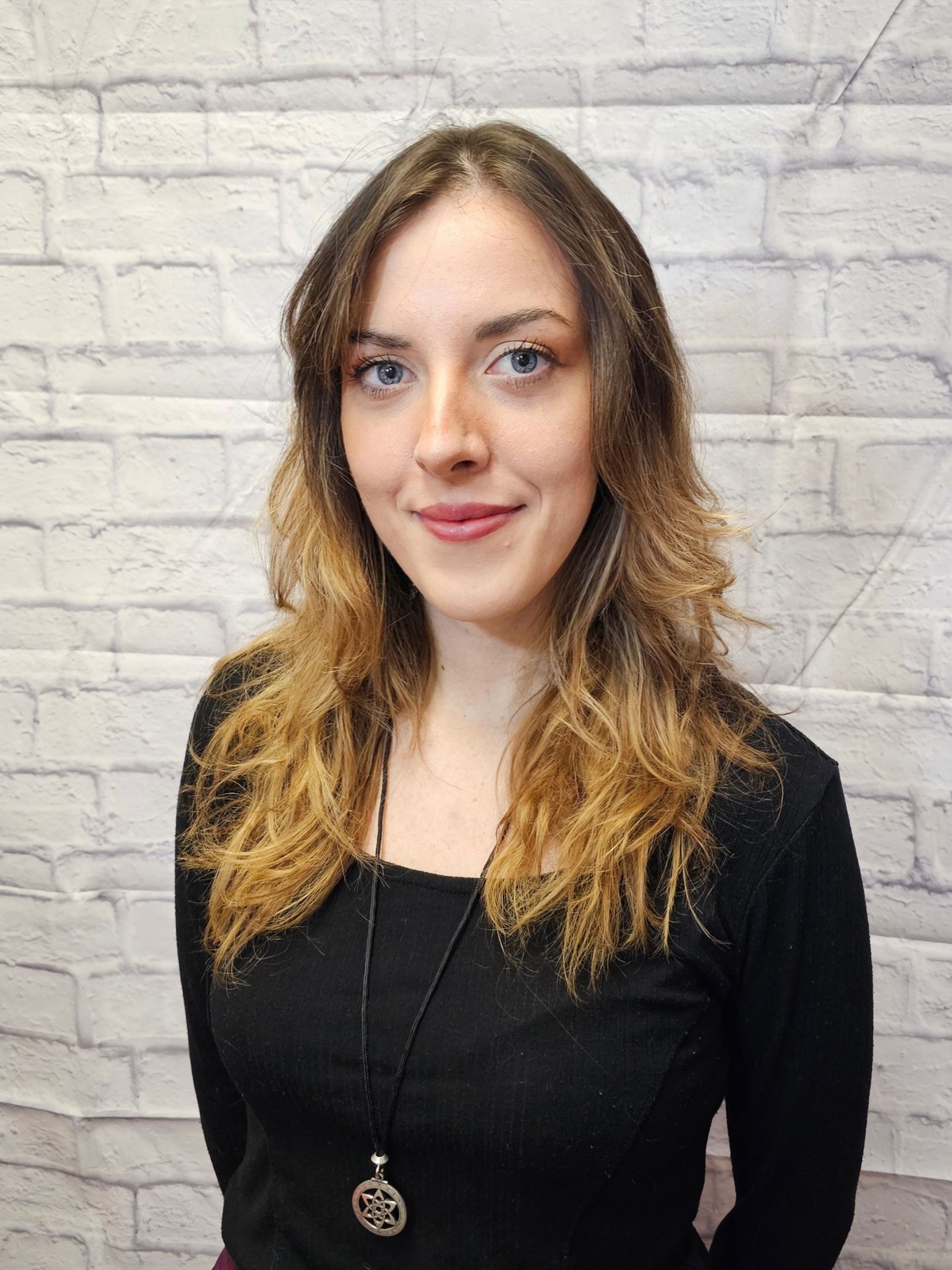 A woman wearing a yellow shirt and a name tag is smiling.
