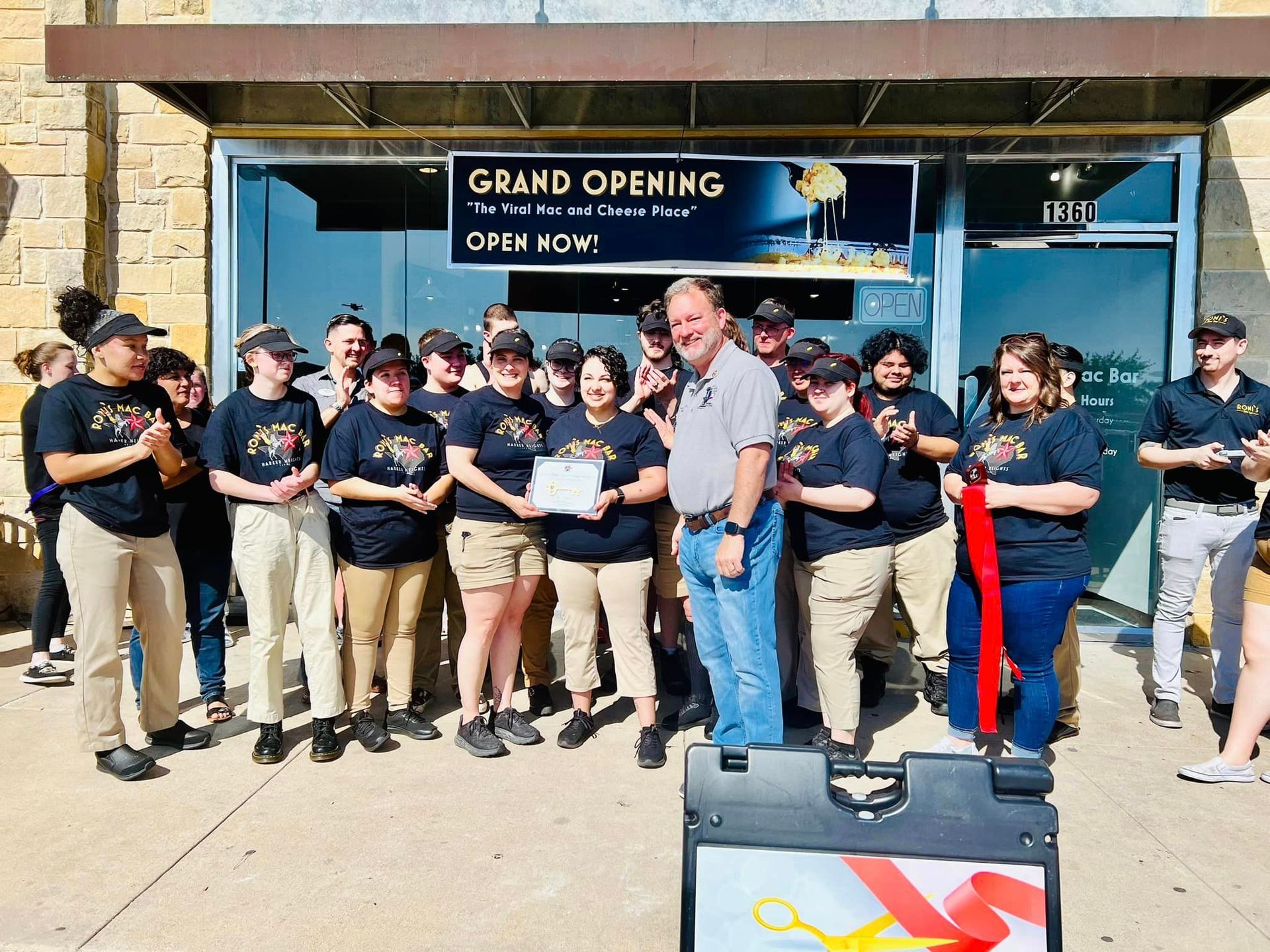 A group of people are standing in front of a building with a sign that says grand opening.