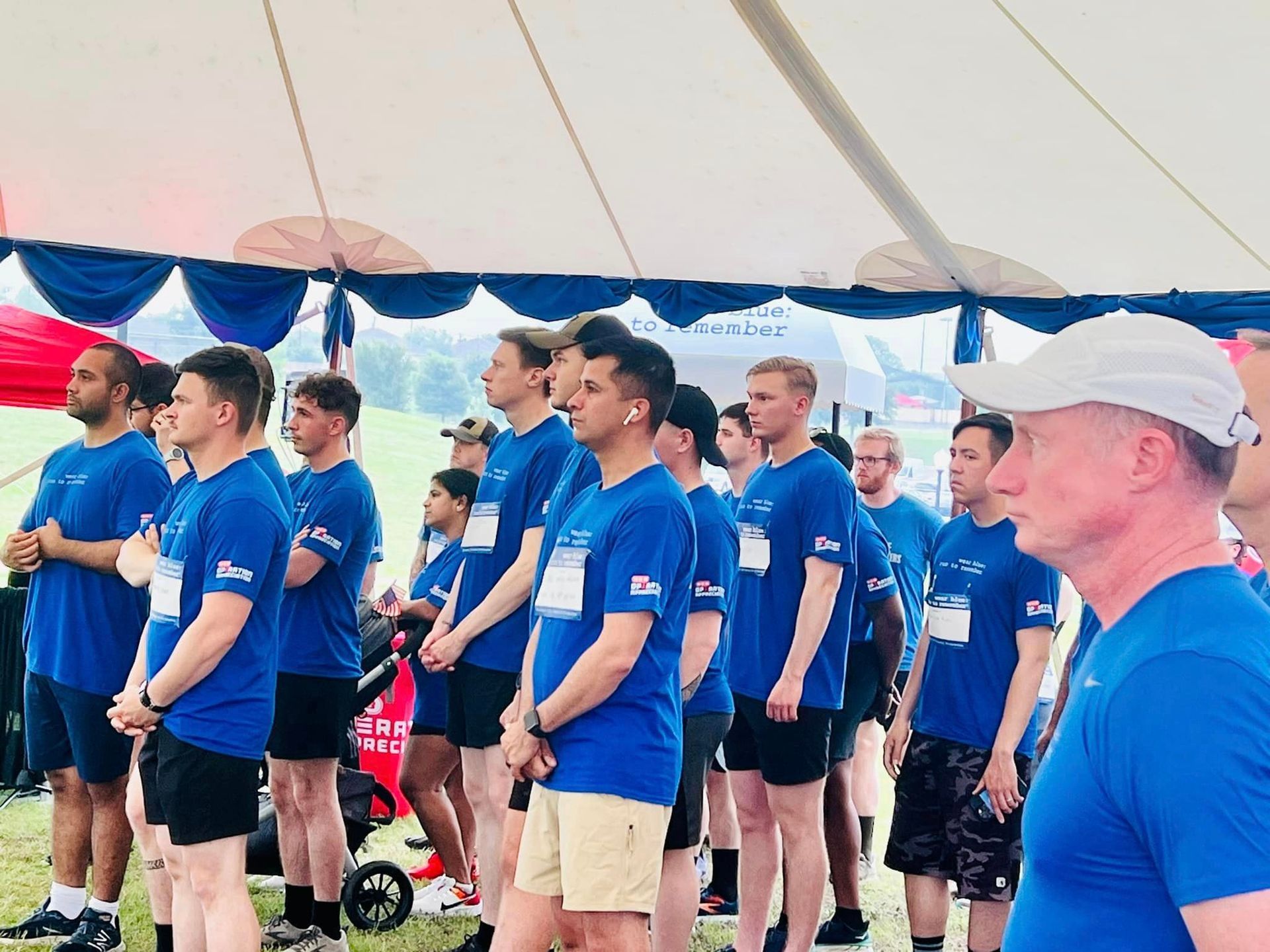 A group of men in blue shirts are standing under a tent.
