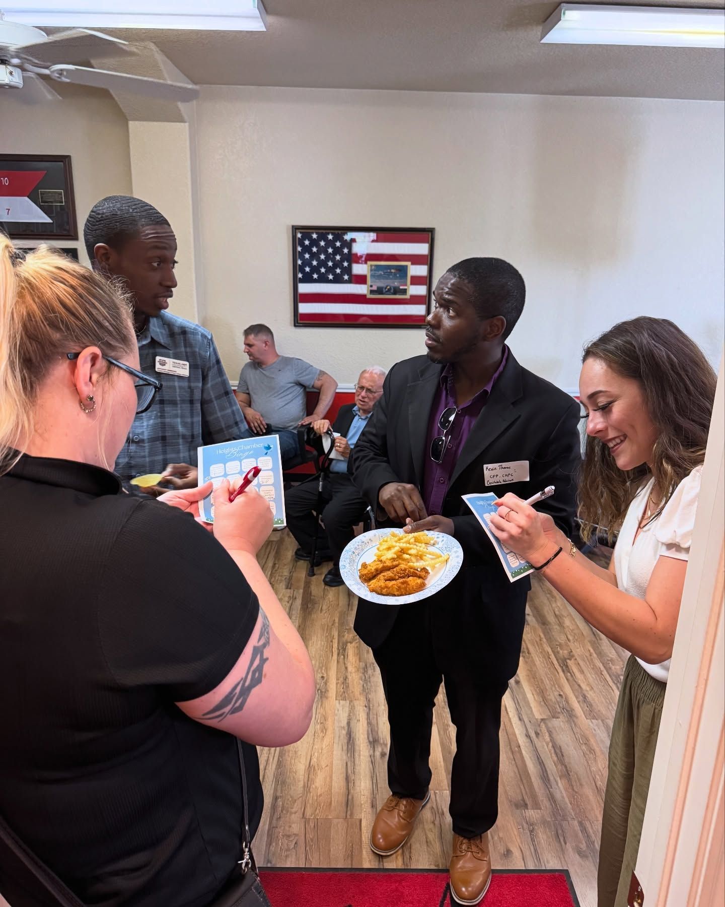 A group of people are standing around a man holding a plate of food.