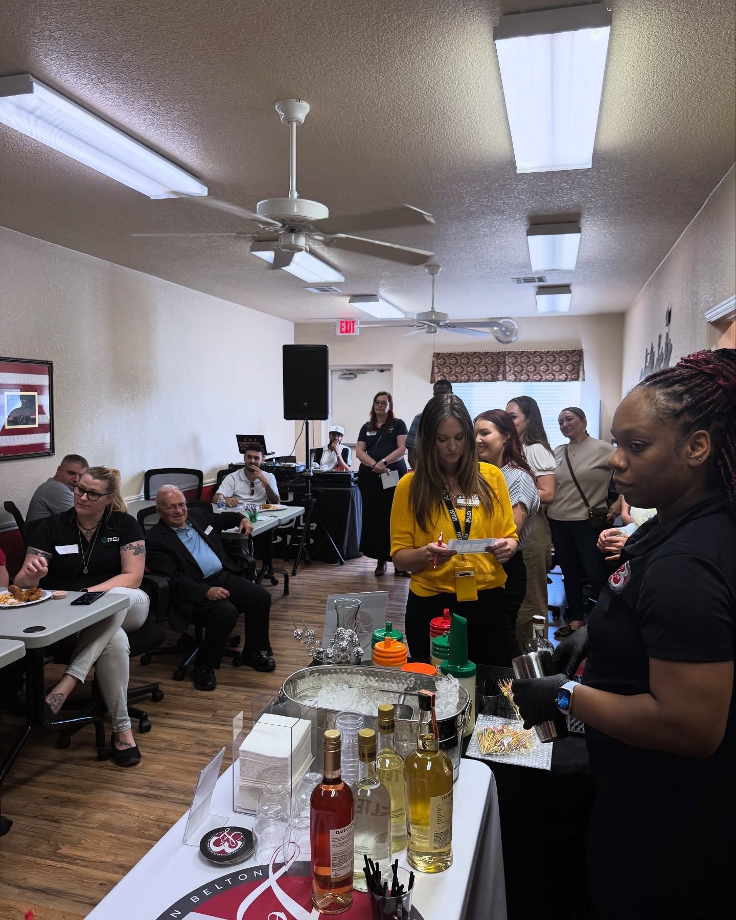 A group of people are standing around a table with bottles of alcohol on it.