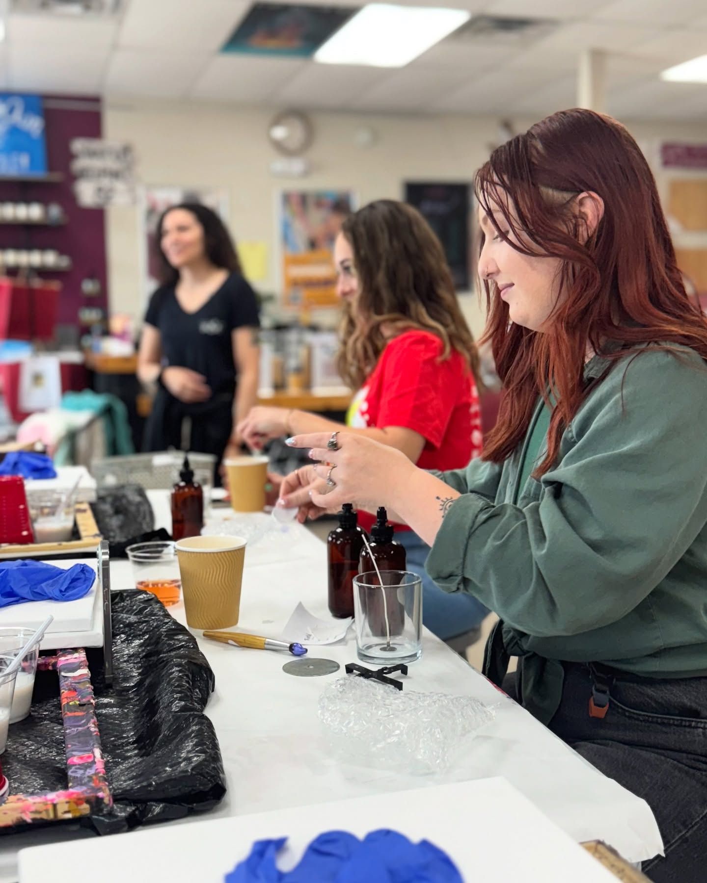 A group of women are sitting at a table making candles.