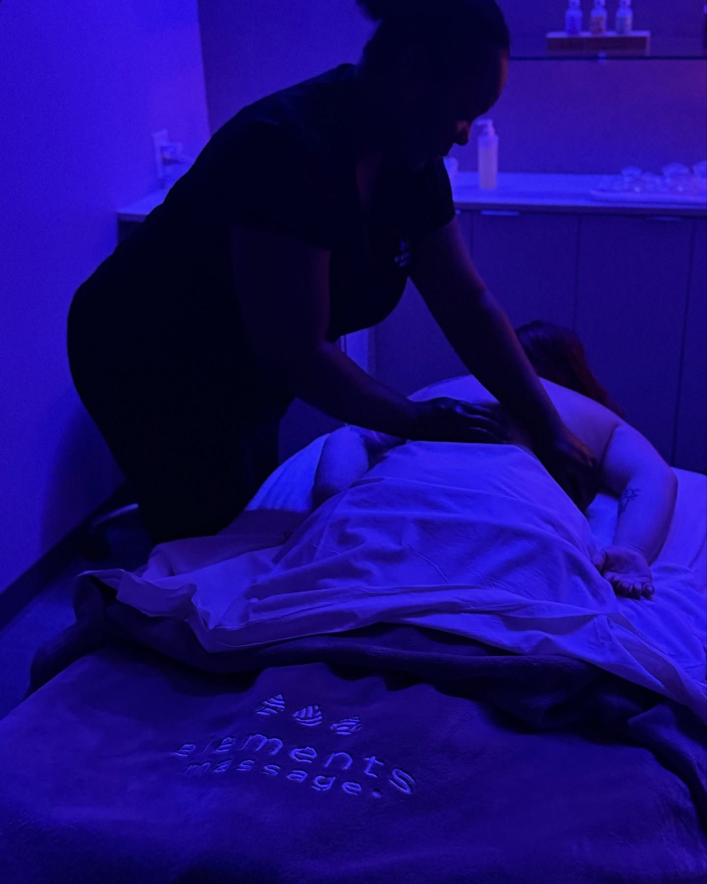 A woman is giving a massage to another woman in a dark room.