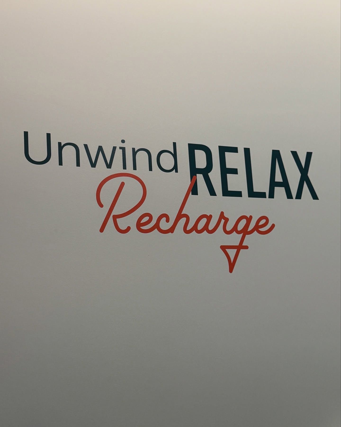 A sign on a wall that says unwind relax recharge