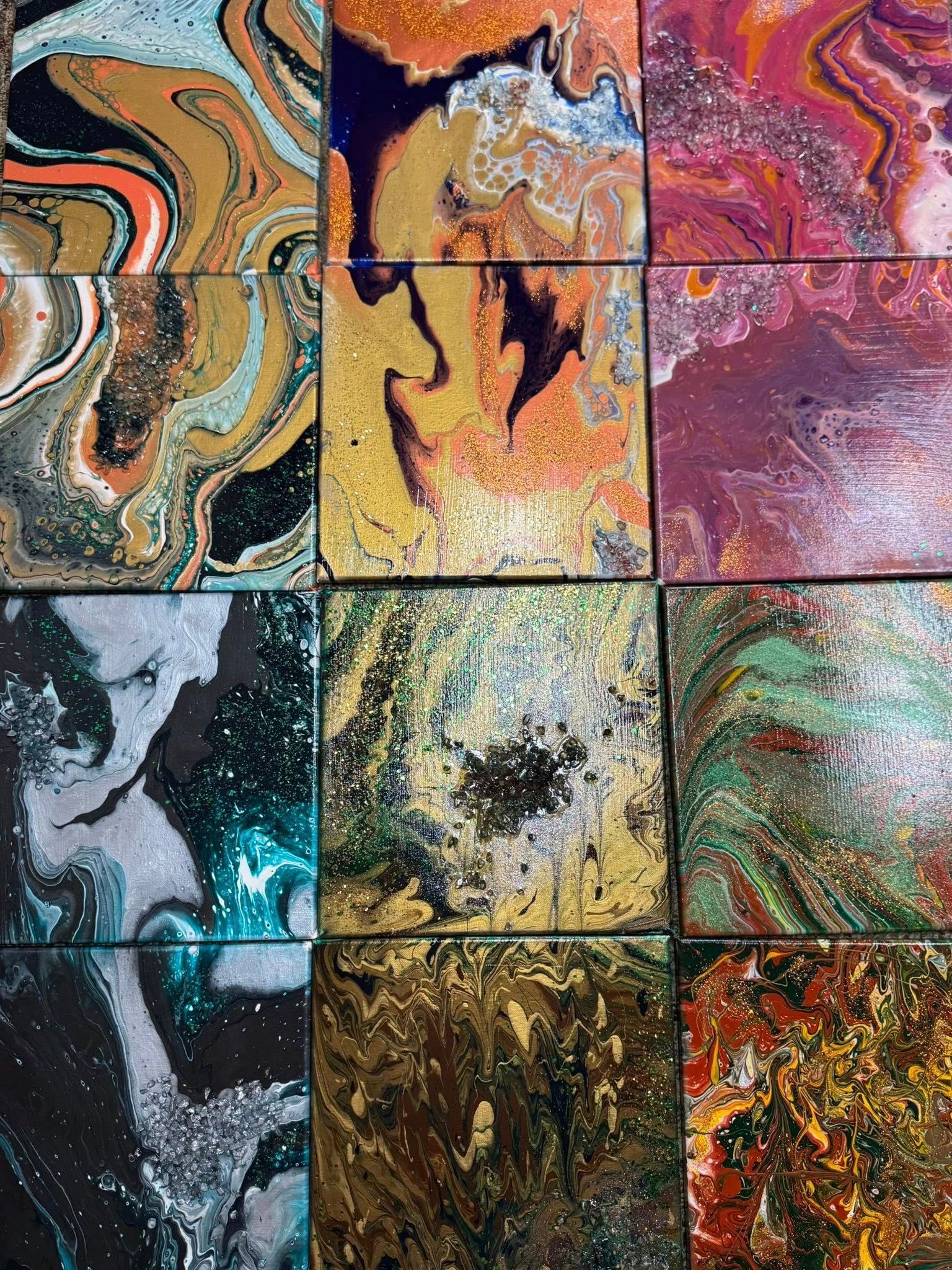 12 canvases of pour art are displayed on the table like a collage.