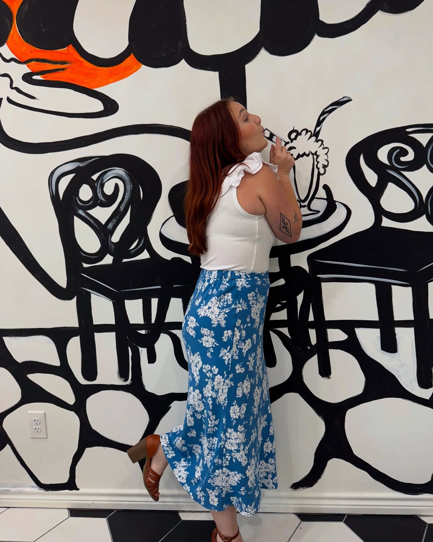 A woman in a blue skirt is standing in front of a mural on a wall.
