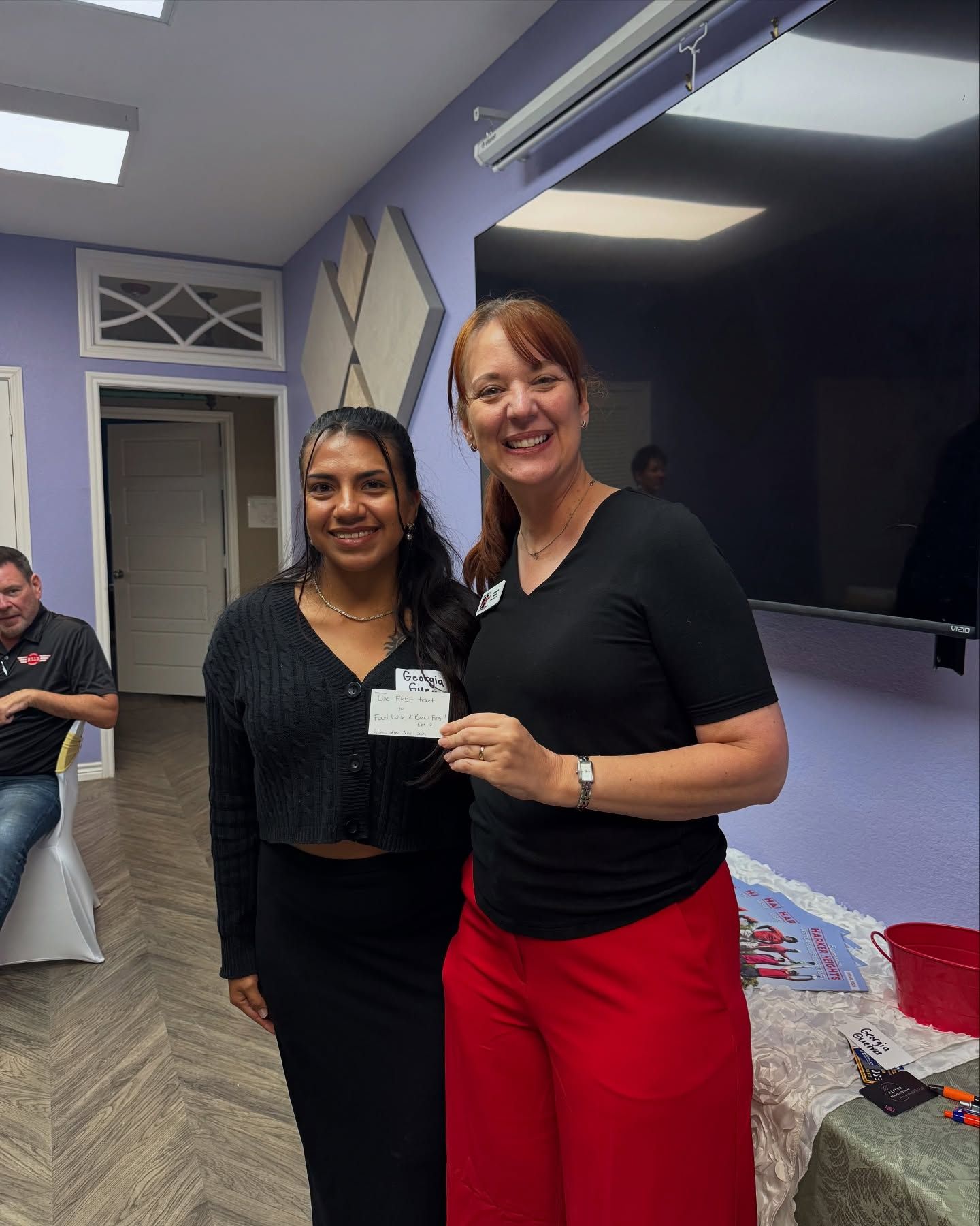 Two women are standing next to each other in a room and smiling.