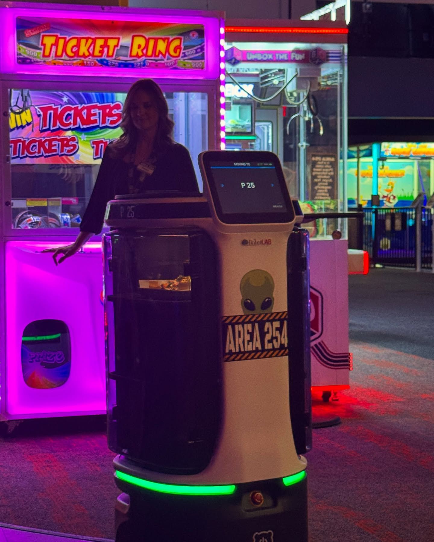A woman stands behind a food delivery robot