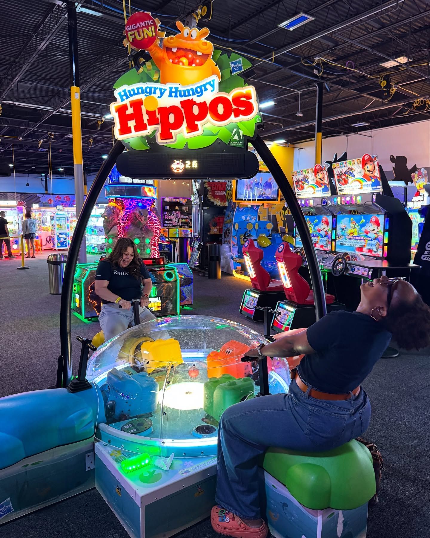 2 women are playing on a giant version of hungry hungry hippos in an arcade.