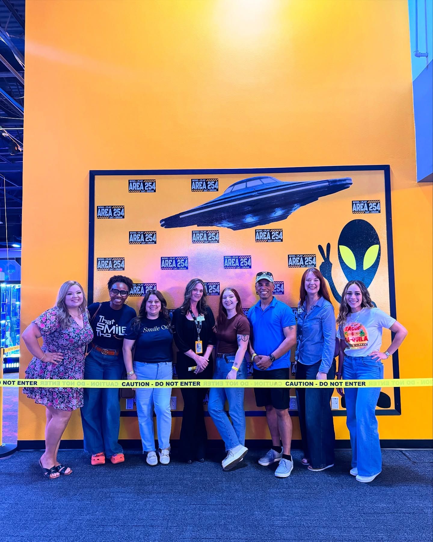 A group of people are posing for a picture in front of an alien mural.