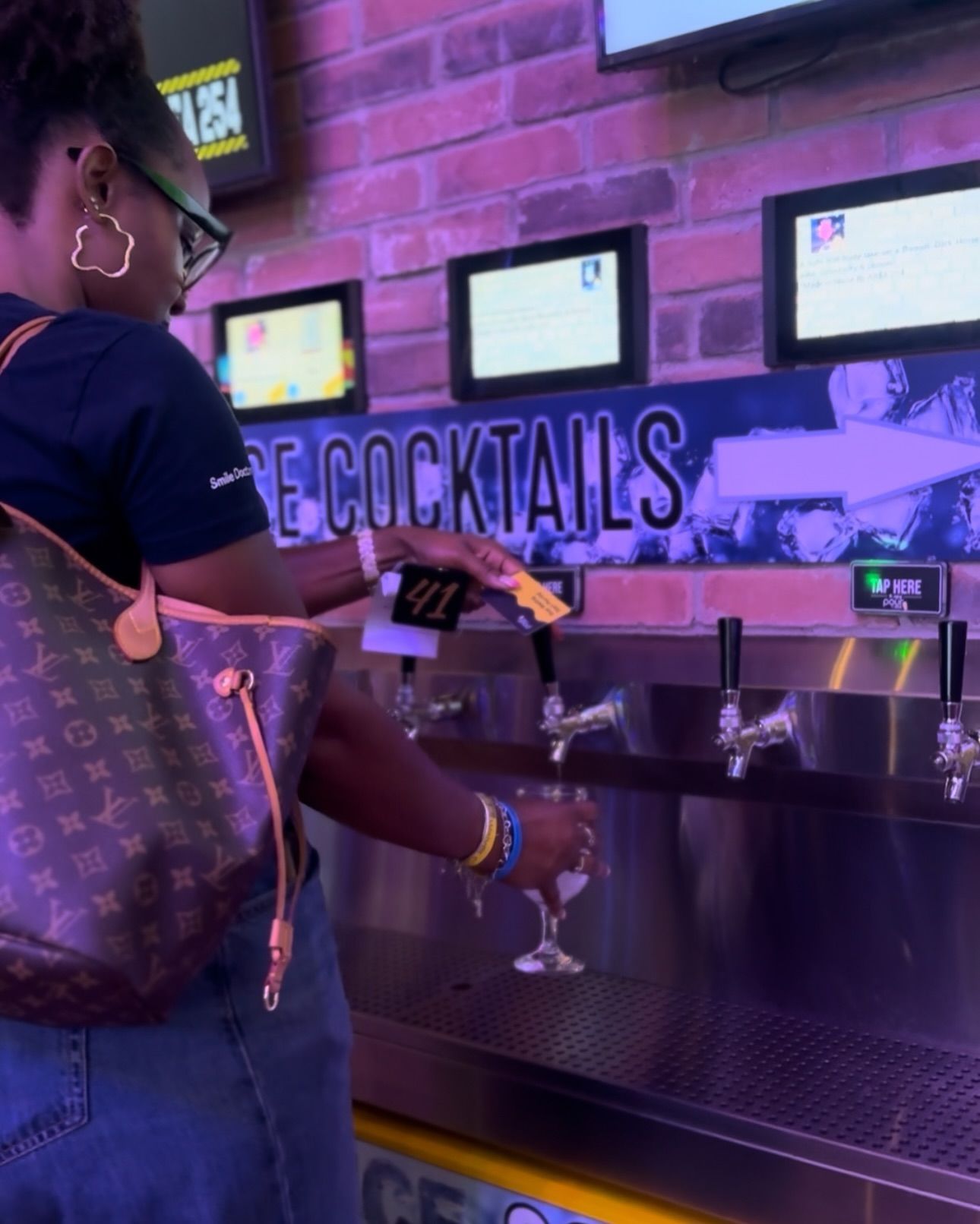 A woman pouring a drink into a glass in front of a sign that says cocktails