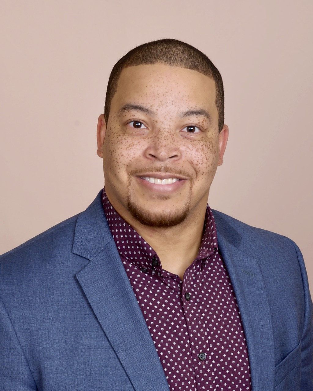 A man in a suit and polka dot shirt is smiling for the camera.