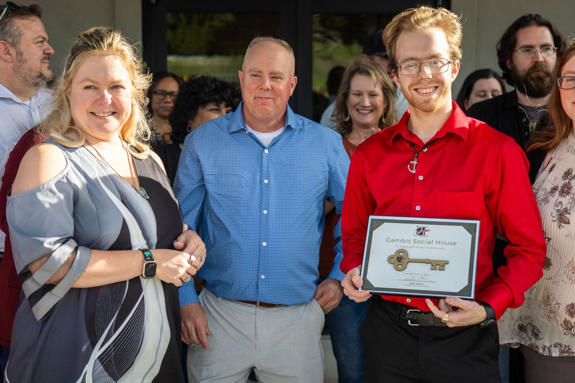 A man in a red shirt is holding a certificate in front of a group of people.