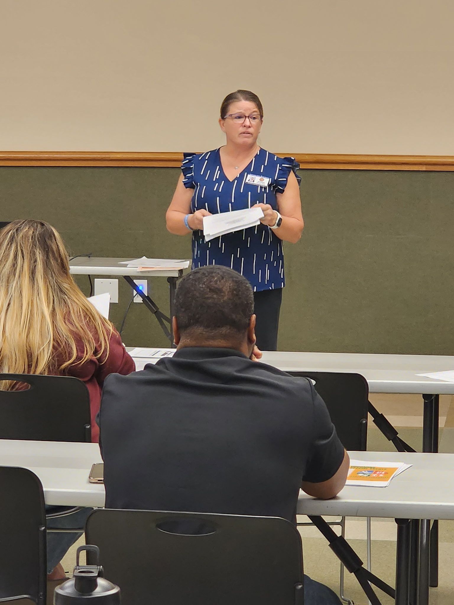 A woman is standing in front of a group of people sitting at tables.