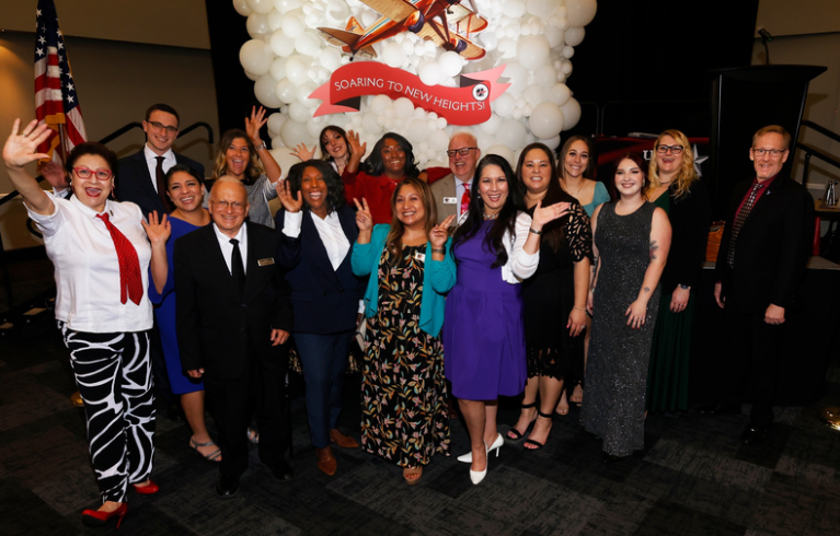 A group of people are standing in front of a building holding a ribbon.