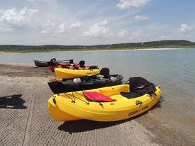 Three yellow kayaks are sitting on the shore of a lake.