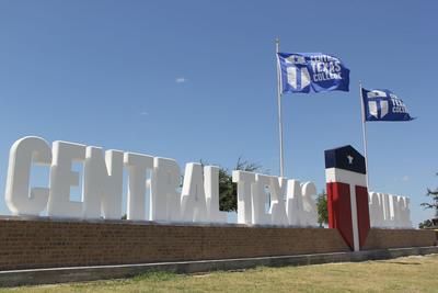 Three flags are flying in front of a large sign that says central texas